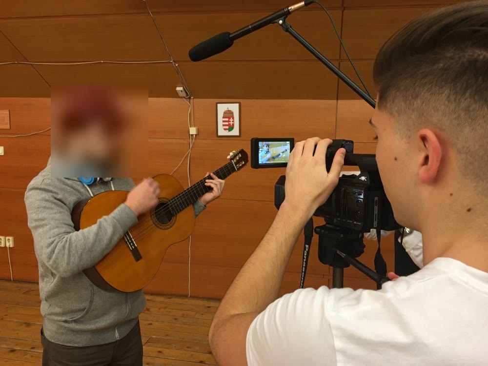 A fiatal Bálint kamerával forgat egy teremben, egy gitáros zenészről